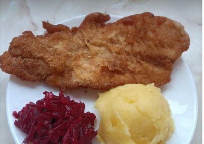 Panierowany kotlet z puree ziemniaczanym i duszoną czerwoną kapustą na talerzu.