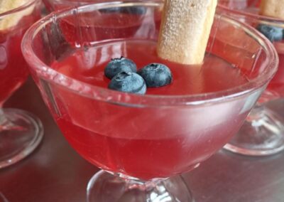 Pucharki z czerwonym deserem, biszkoptem i jagodami na wierzchu.