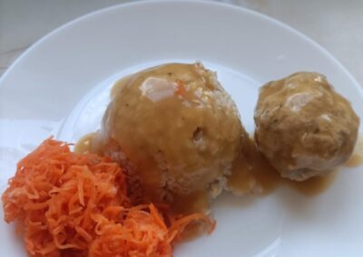 Dwa pulpety z sosem i surówka z marchewki na białym talerzu.