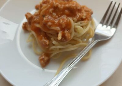 Porcja spaghetti z sosem pomidorowym na talerzu, z widelcem, na jasnym tle.