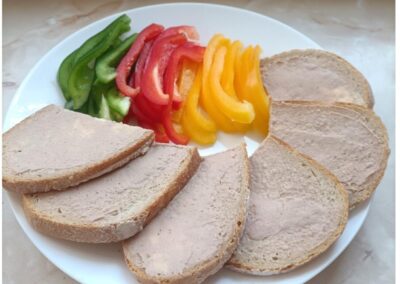 Talerz z chlebem z pasztetem i paskami zielonej, czerwonej, żółtej papryki.